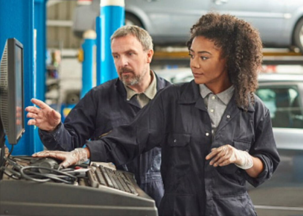 2 mechanics sorting information on a computer in vehicle repair shop